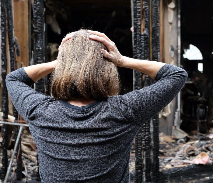 Woman with hands on her head looking at burnt down house